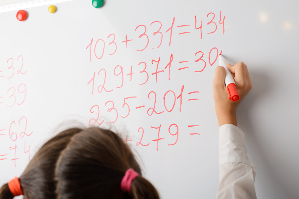 Young child writing maths exercises on whiteboard in class